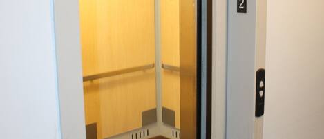 An elevator with a wooden interior, a door with a number plate, and a sign indicating a smoking area.