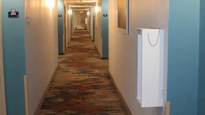 Un couloir d'hôtel avec des revêtements de sol en moquette, des murs bleu clair et des portes numérotées.