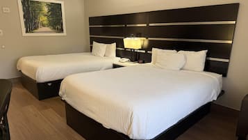 Quarto de hotel com duas camas, mesa de cabeceira com abajur, um quadro na parede e chão de madeira.
