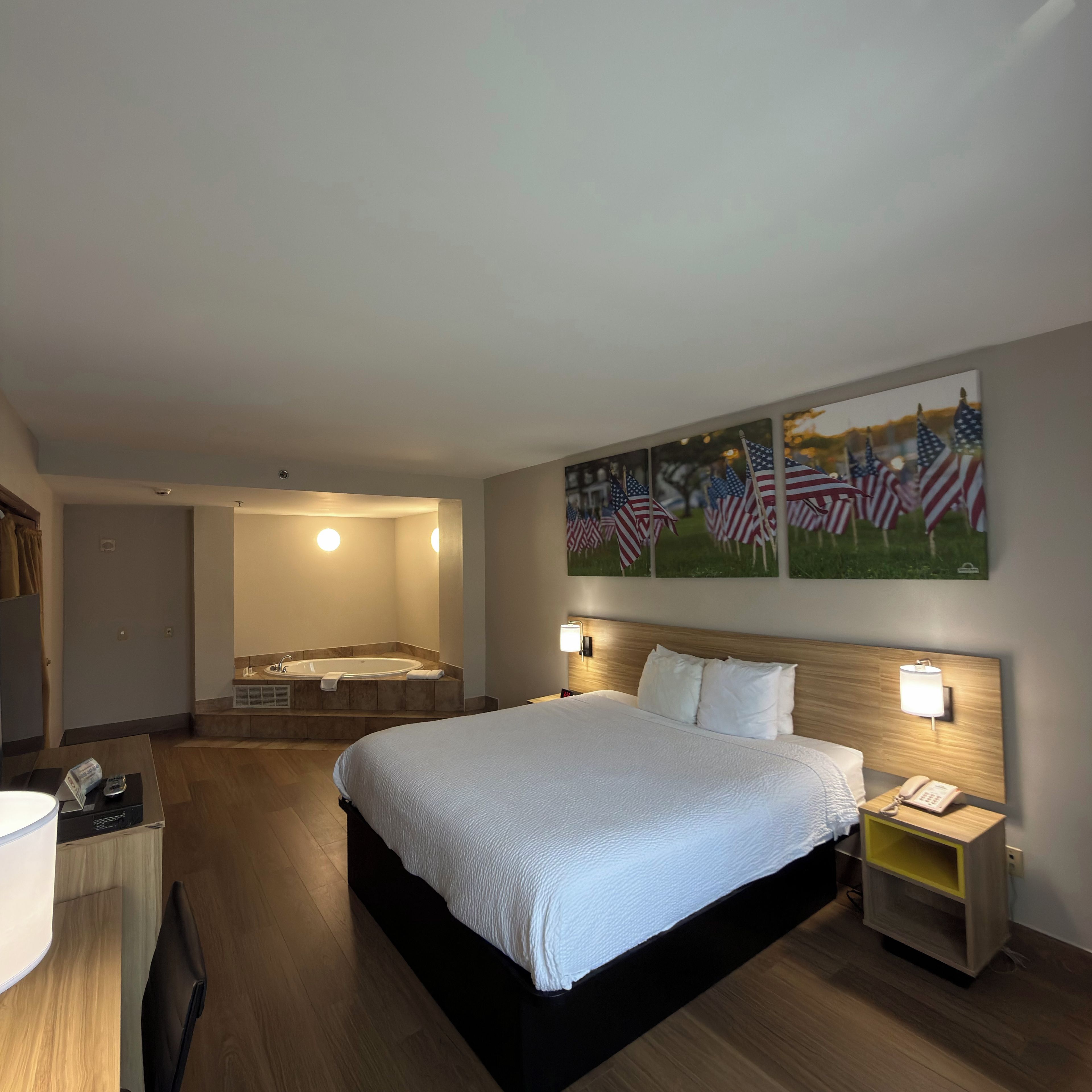 Une chambre d’hôtel avec un grand lit, une salle de bain avec une baignoire et un mur décoré de tableaux représentant le drapeau américain.