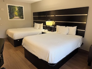 Een hotelkamer met twee bedden, een nachtkastje met een lamp, een telefoon en een schilderij van een bos aan de muur.