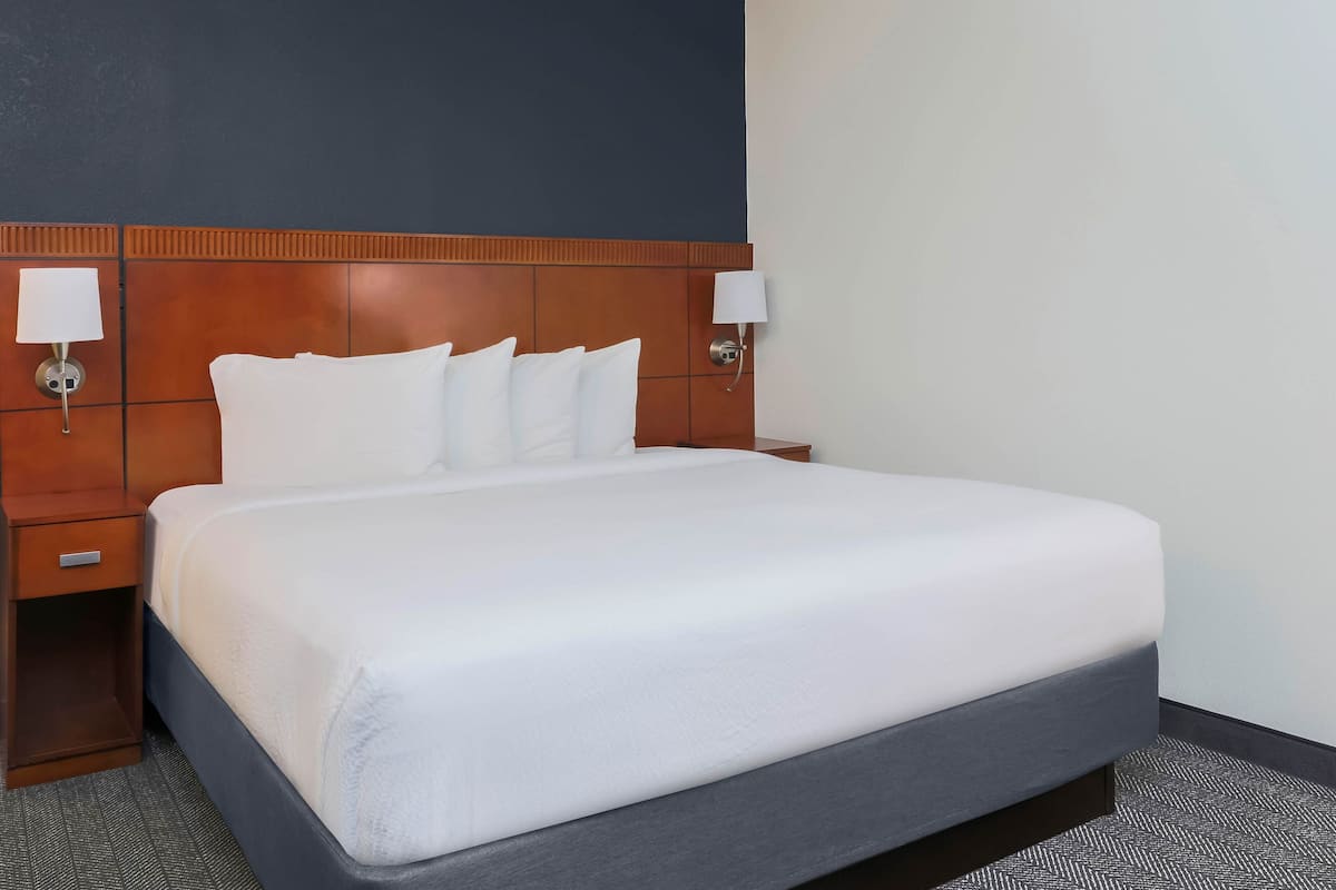 A hotel room with a large bed, wooden headboard, two bedside tables, and wall-mounted lamps.