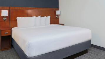 A hotel room with a large bed, wooden headboard, two bedside tables, and wall-mounted lamps.