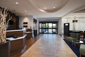 A spacious lobby with a reception desk, seating area, and large windows offering a view of the outdoors. - Courtyard by Marriott Austin Airport (Austin)