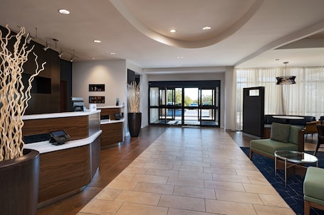 A spacious lobby with a reception desk, seating area, and large windows offering a view of the outdoors.