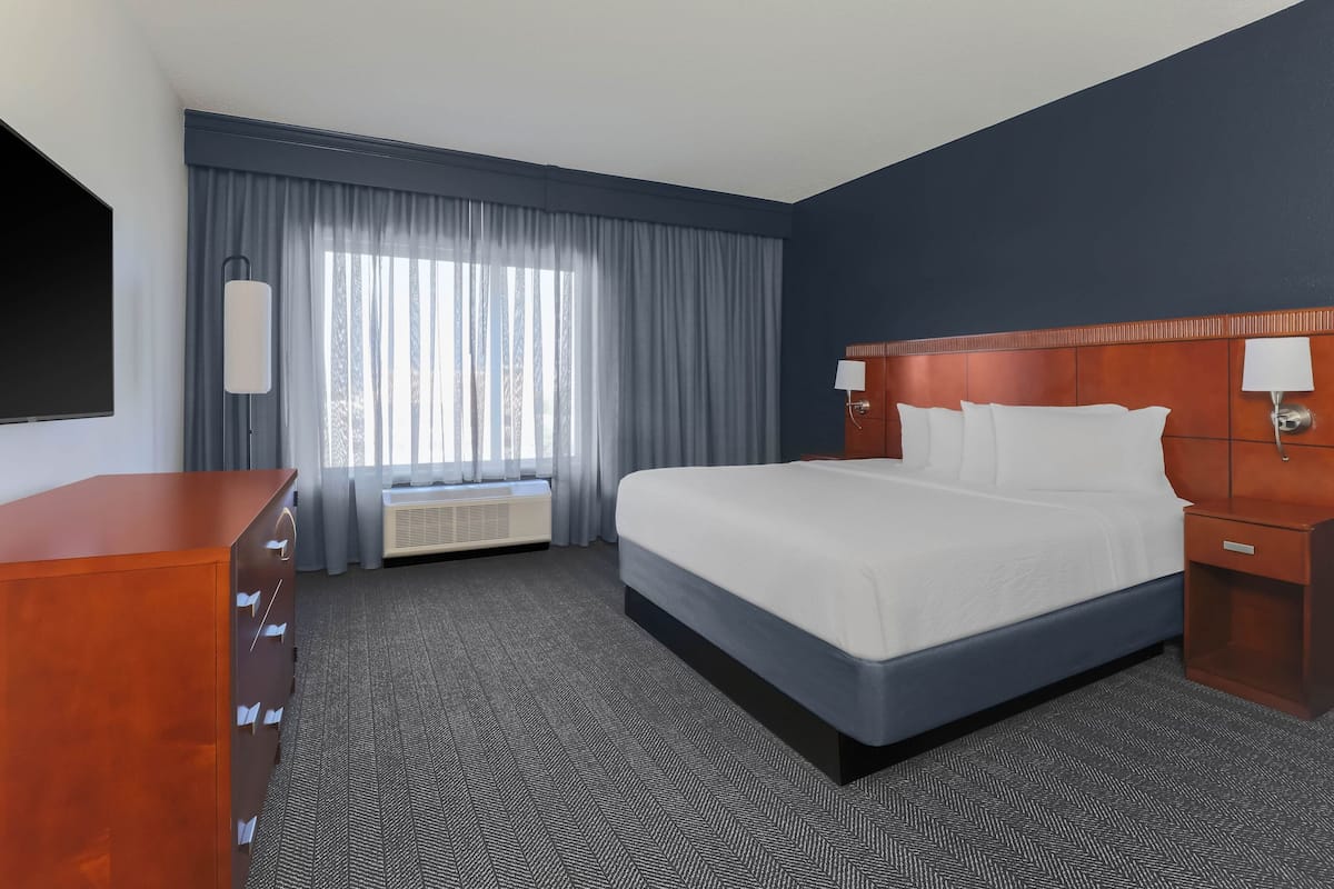 A hotel room with a large bed, a wooden dresser, a flat-screen TV, and a window with curtains.