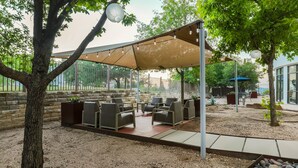 An outdoor seating area with a canopy, surrounded by trees and a stone wall. - Courtyard by Marriott Austin Airport (Austin)