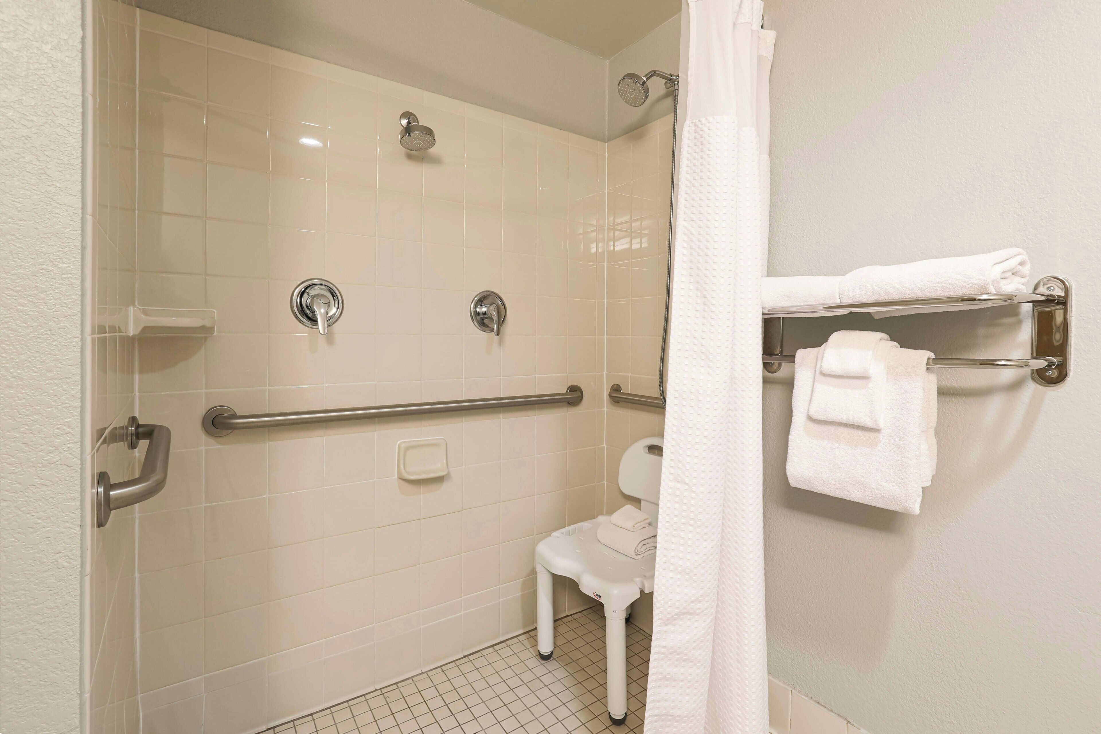 A bathroom with a shower, grab bars, a toilet, and a towel rack.