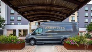 A Courtyard by Marriott van parked under a covered area with a brick pathway and flower planters. - Courtyard by Marriott Austin Airport (Austin)