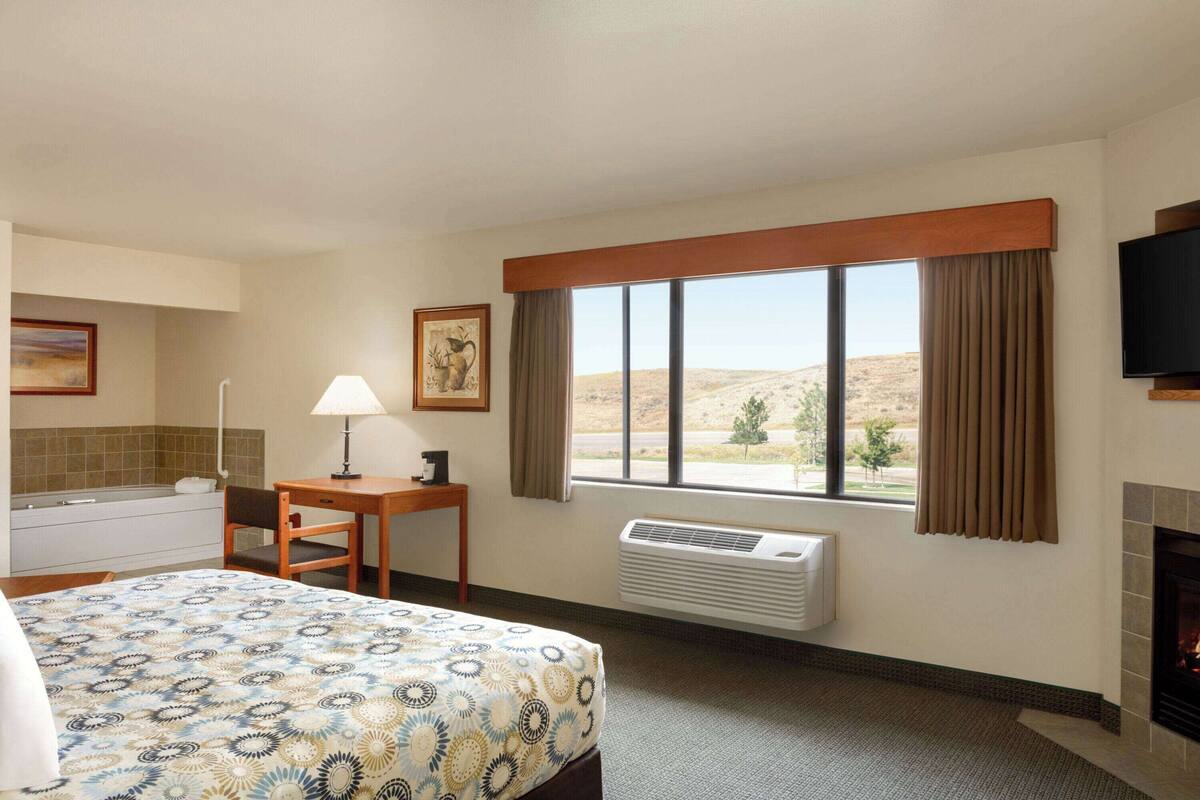 A hotel room with a bed, a desk, a chair, a window with a view of the desert, a television, and a fireplace.