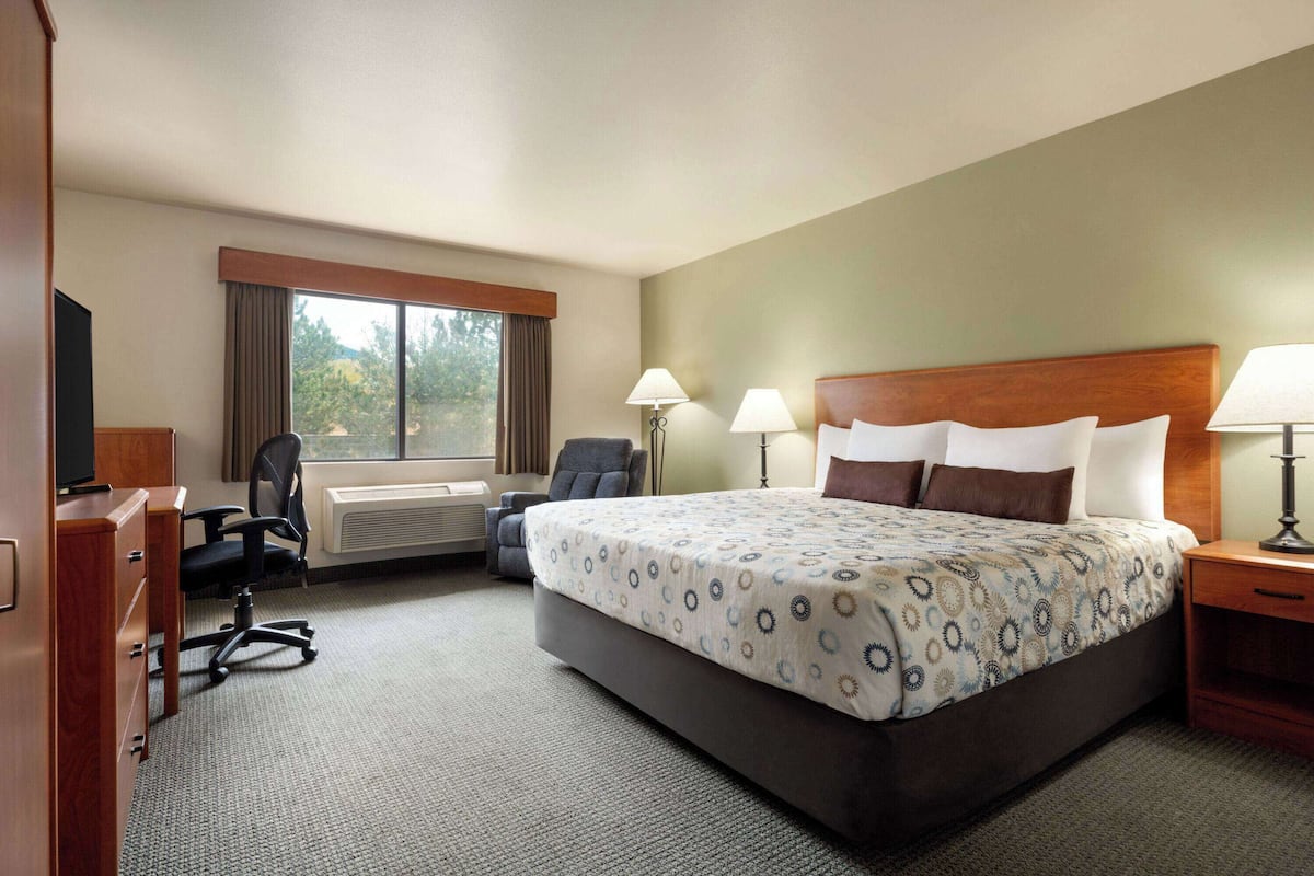 A hotel room with a large bed, two bedside lamps, a desk with a chair, and a window with curtains.