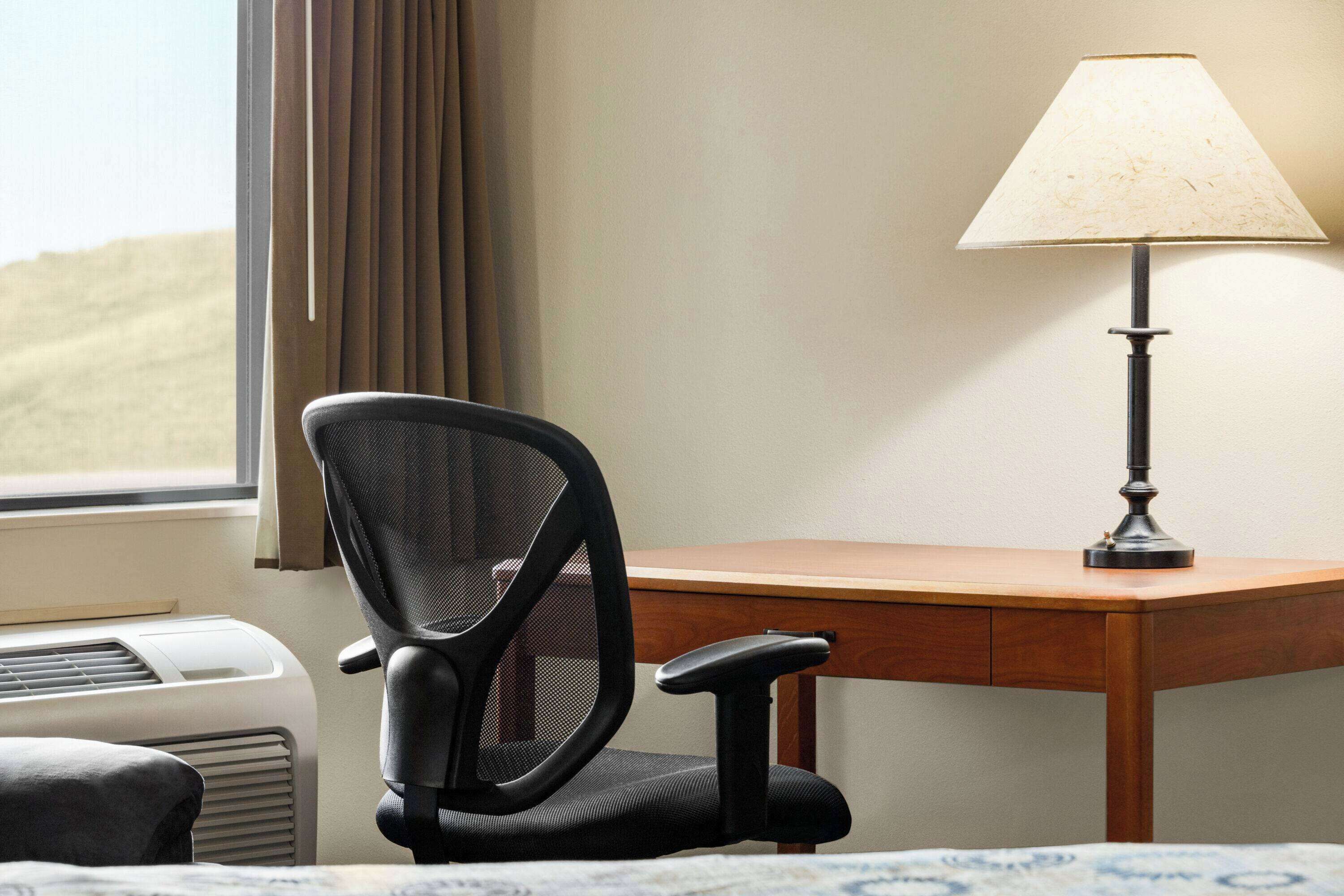 Hotelkamer met een bureau, stoel, lamp, airconditioning en uitzicht op de woestijn door het raam.