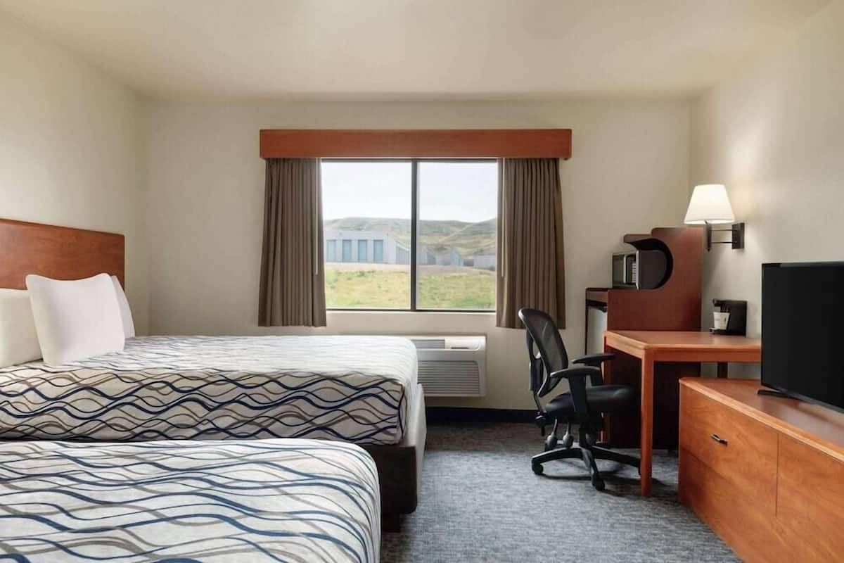 A hotel room with a bed, a desk, a chair, a TV, and a window with curtains.