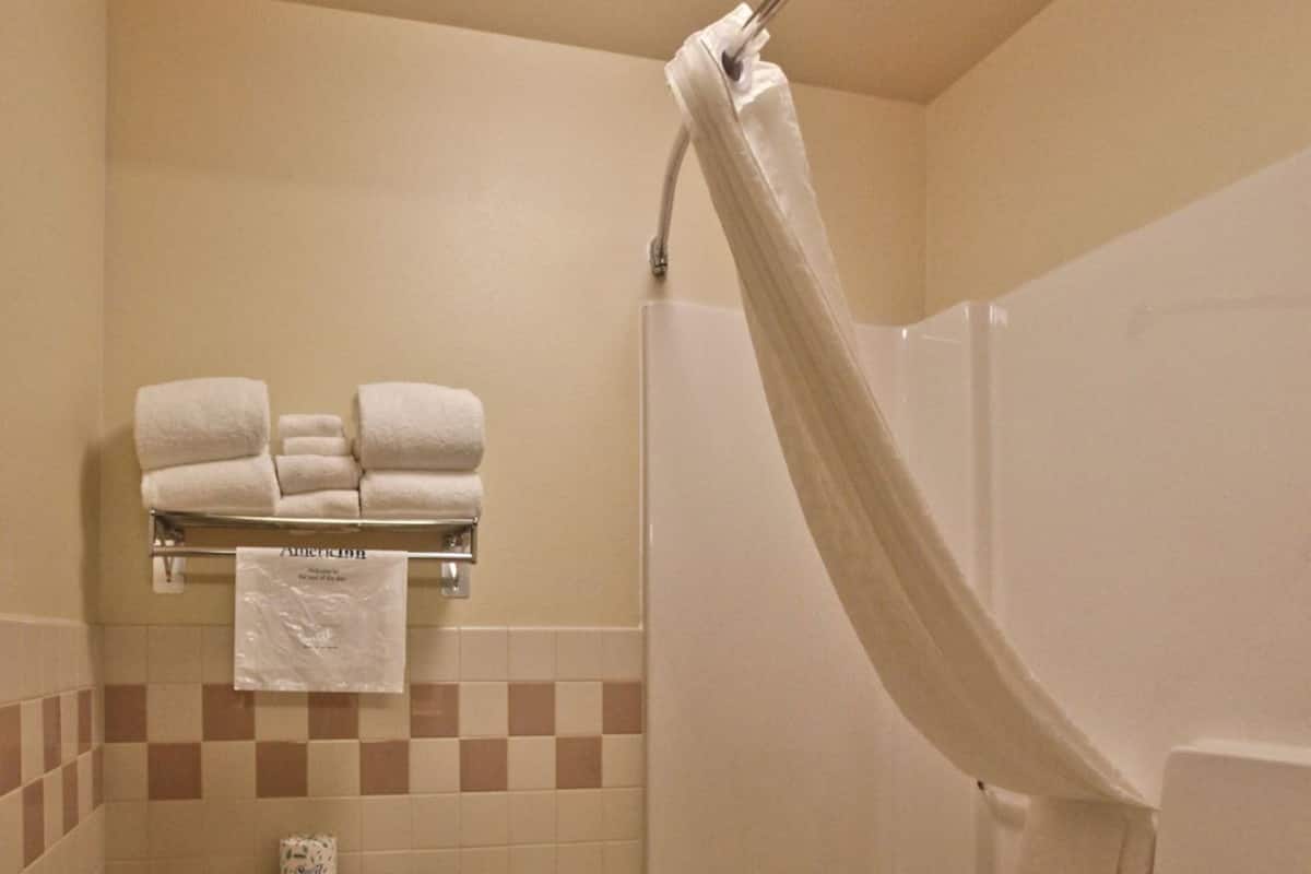 A bathroom with a toilet, a shower with a curtain, and a towel rack with towels.