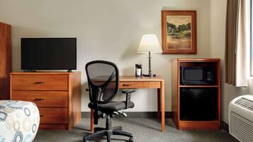 A hotel room with a bed, a desk with a computer, a chair, a television, a lamp, a microwave, and a heater.
