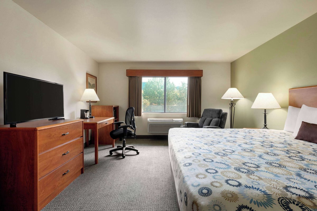 A hotel room with a bed, desk, chair, television, and window.
