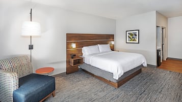 A modern hotel room with a large bed, a small round table, a sofa, and a wall-mounted lamp.