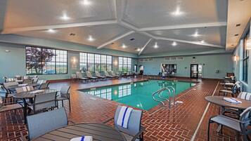 An indoor pool area with lounge chairs and tables, a pool, and a view of the outdoors.