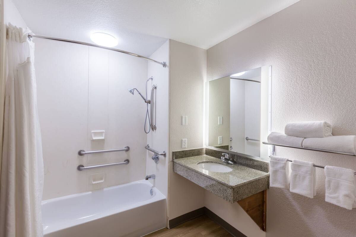 A bathroom with a bathtub, a sink, a mirror, and a towel rack.