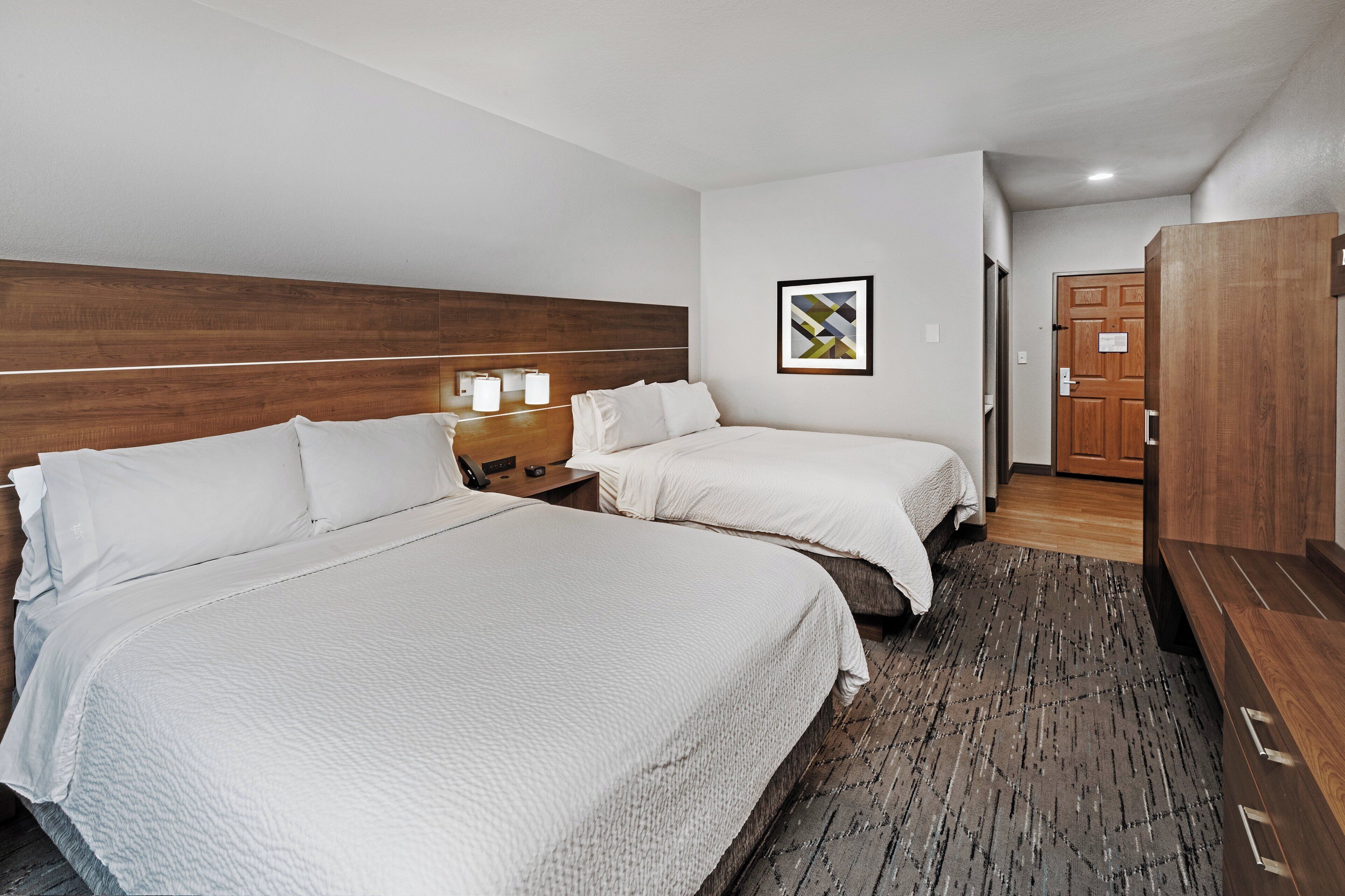 A hotel room with two beds, a wooden headboard, a framed picture on the wall, and a wardrobe.
