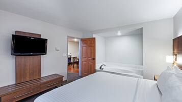 Ett hotellrum med en stor säng, en tv som är monterad på väggen, ett träskåp, ett badkar och ett skrivbord med en stol.