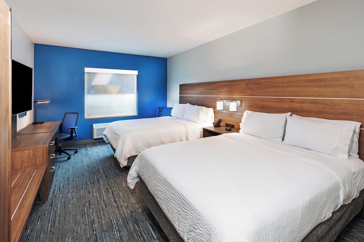 A hotel room with two beds, a desk, a chair, a TV, and a window.
