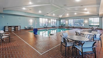 Zona de piscina con suelo de ladrillo, mesas de billar, sillas y vistas al exterior a través de amplios ventanales.