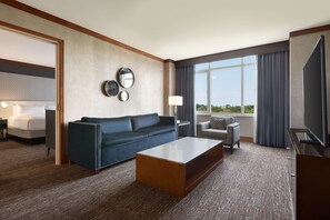 A hotel room with a large bed, a blue sofa, a coffee table, a TV, and a view of the outdoors. - Hilton Baltimore BWI Airport (Linthicum Heights)