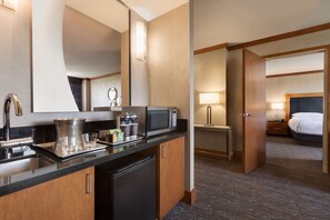 A hotel room with a kitchenette, a bed, a bedside table with a lamp, and a large mirror. - Hilton Baltimore BWI Airport (Linthicum Heights)