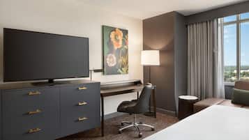 Habitación de hotel con televisión de pantalla plana, escritorio, silla, cama, lámpara y un cuadro en la pared.