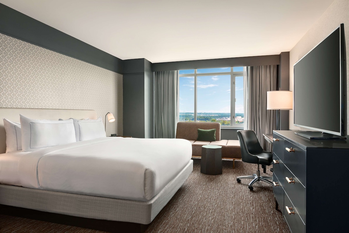 A hotel room with a large bed, a sofa, a TV, and a view of the city.