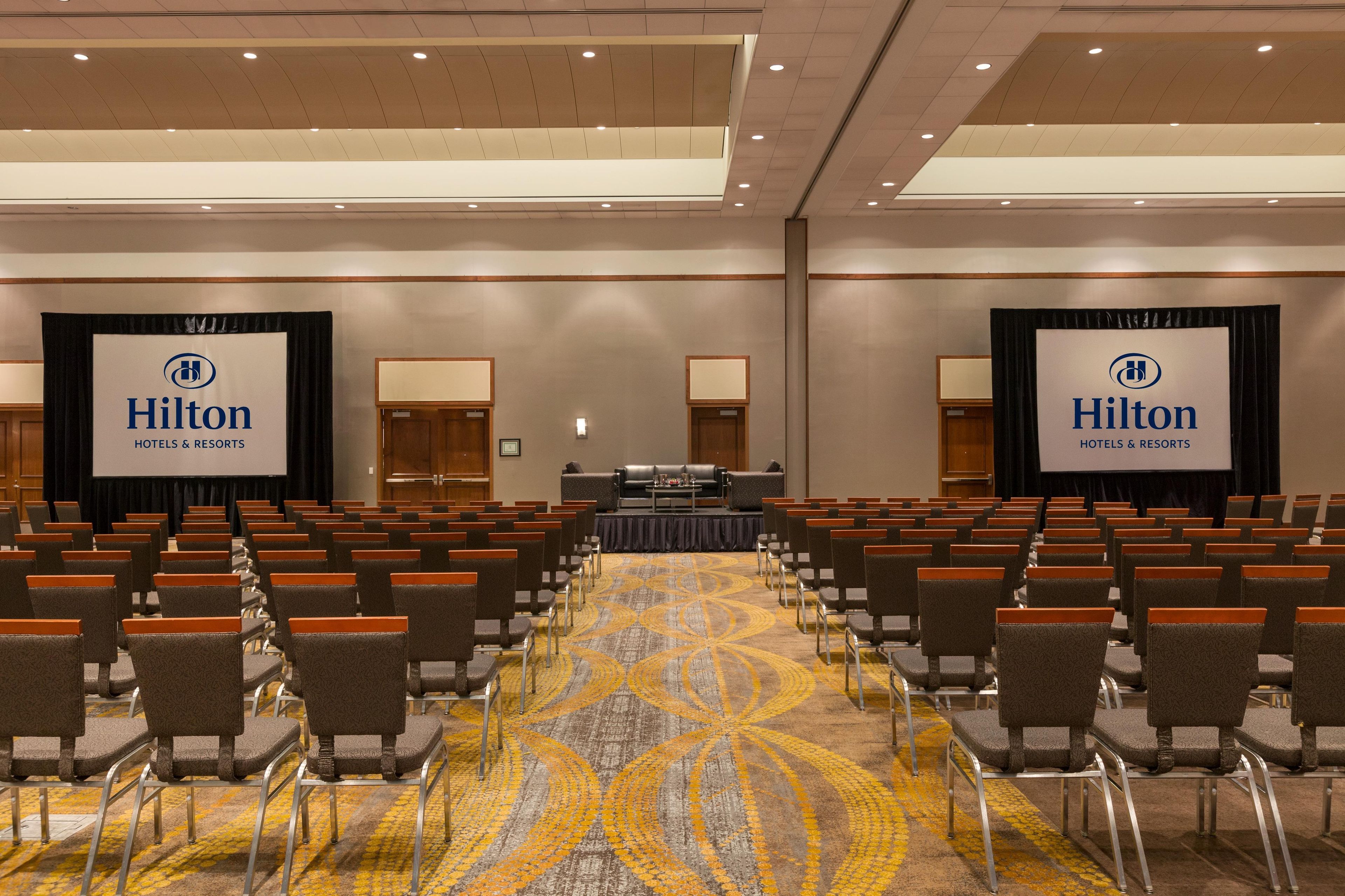 Une salle de conférence avec des rangées de chaises, une scène avec un pupitre et deux grandes banderoles à l’effigie de la marque Hilton.