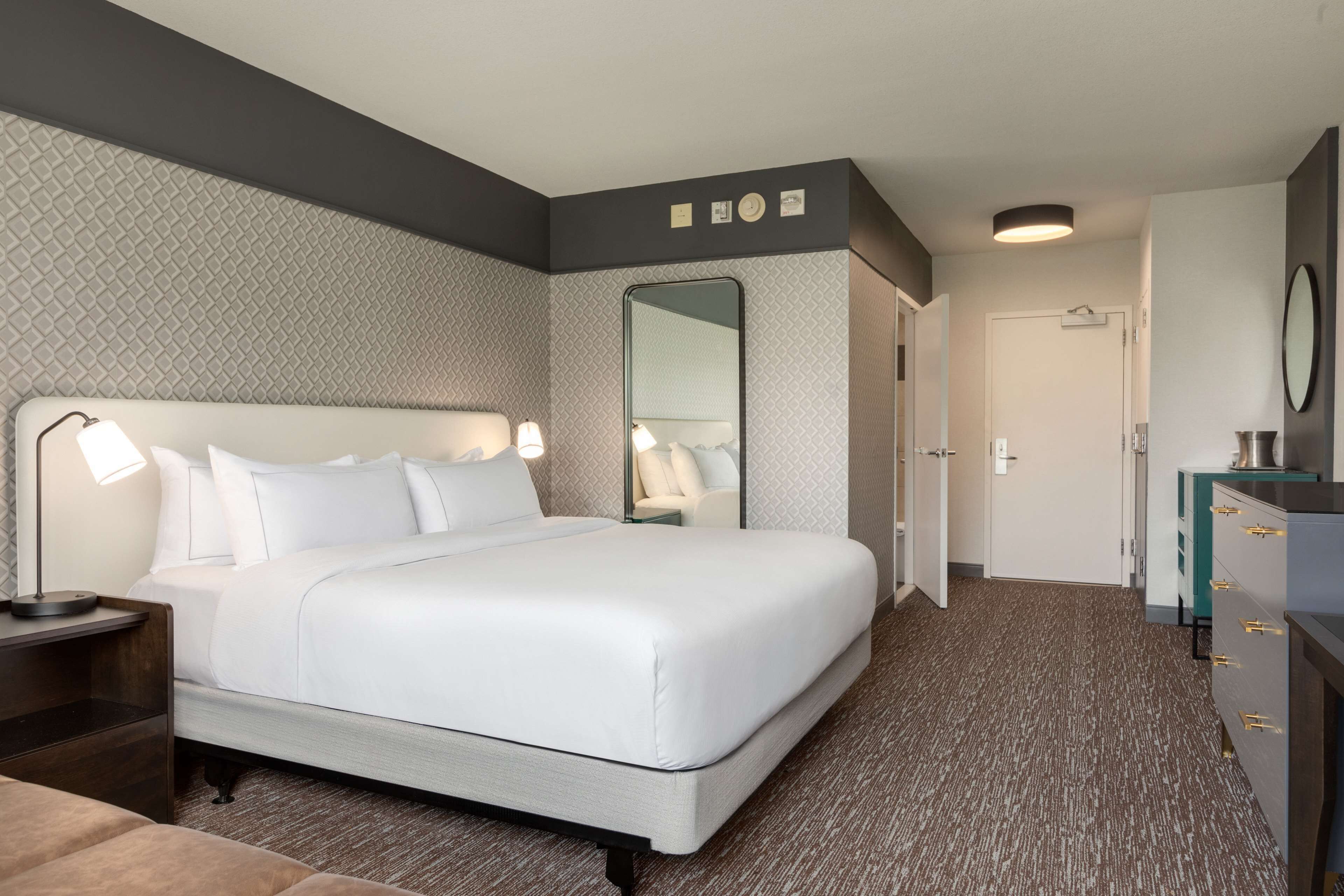 Una habitación de hotel con una cama grande, lámparas de noche, un aparador y un espejo.
