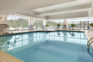 Una amplia piscina interior con agua cristalina, rodeada de ventanas con vistas a árboles.