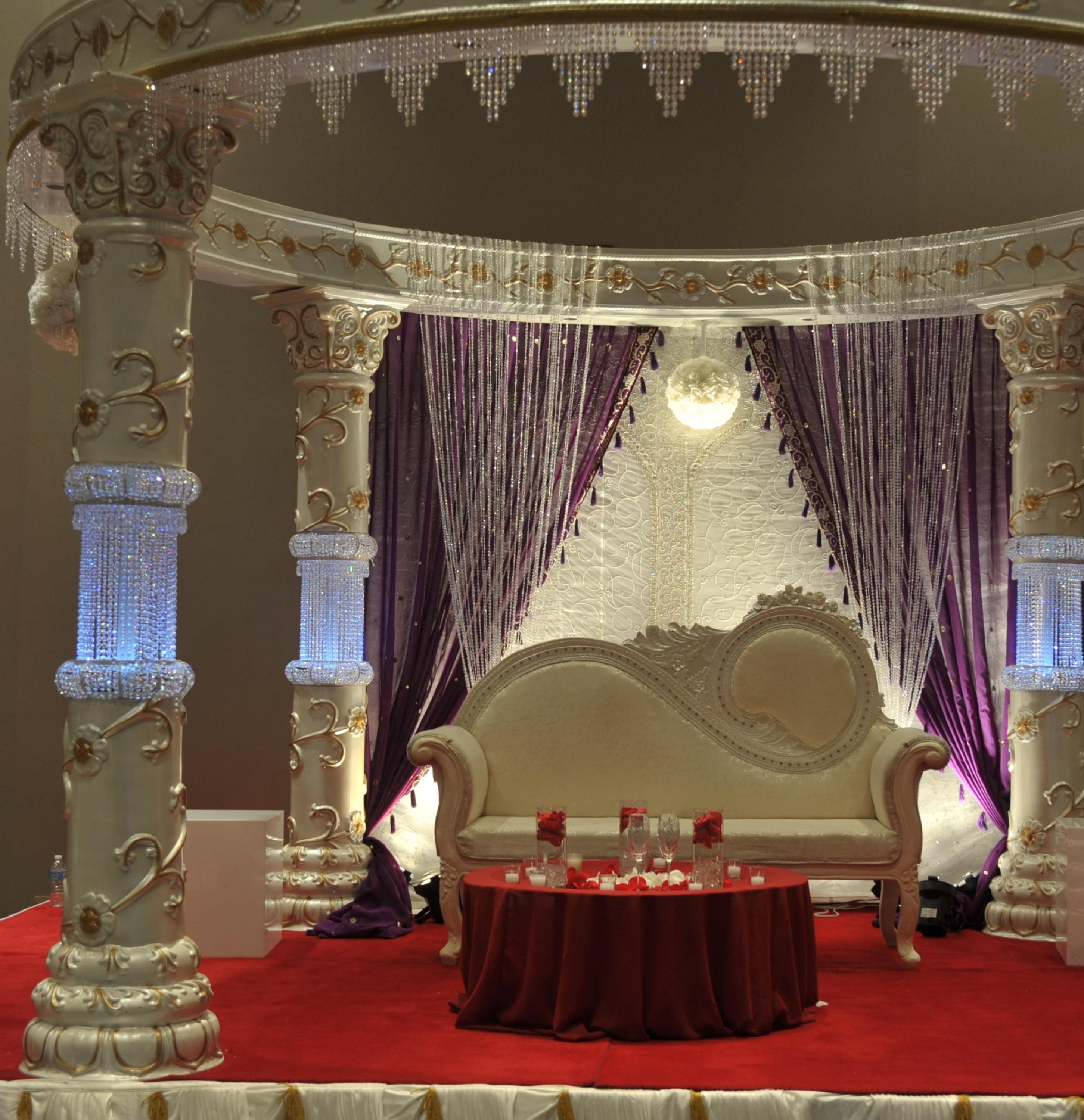 An ornate room with a round table, red carpet, and a decorative backdrop with drapes.