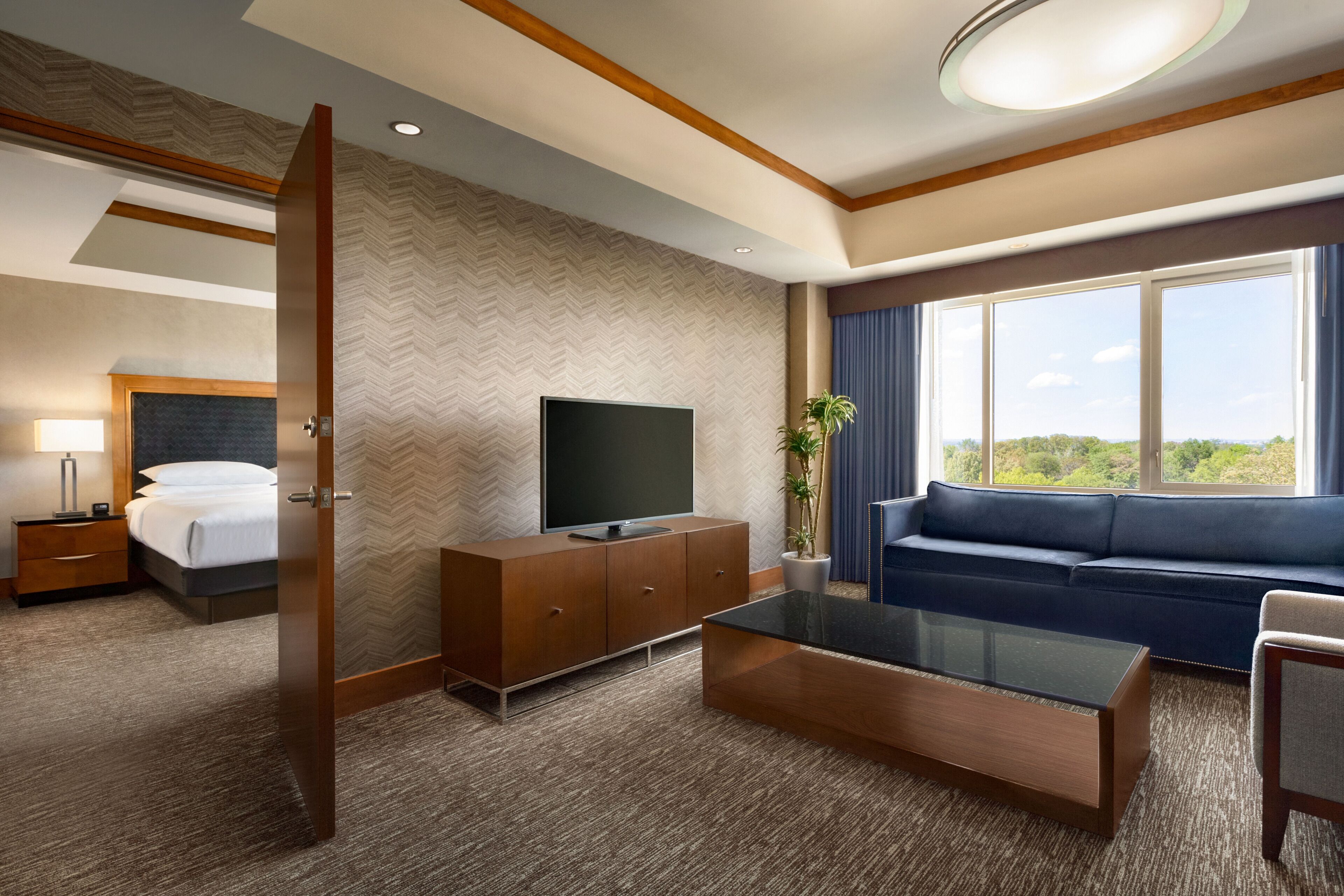 Habitación de hotel con cama, televisor, sofá, mesa de centro y una ventana grande con vistas.