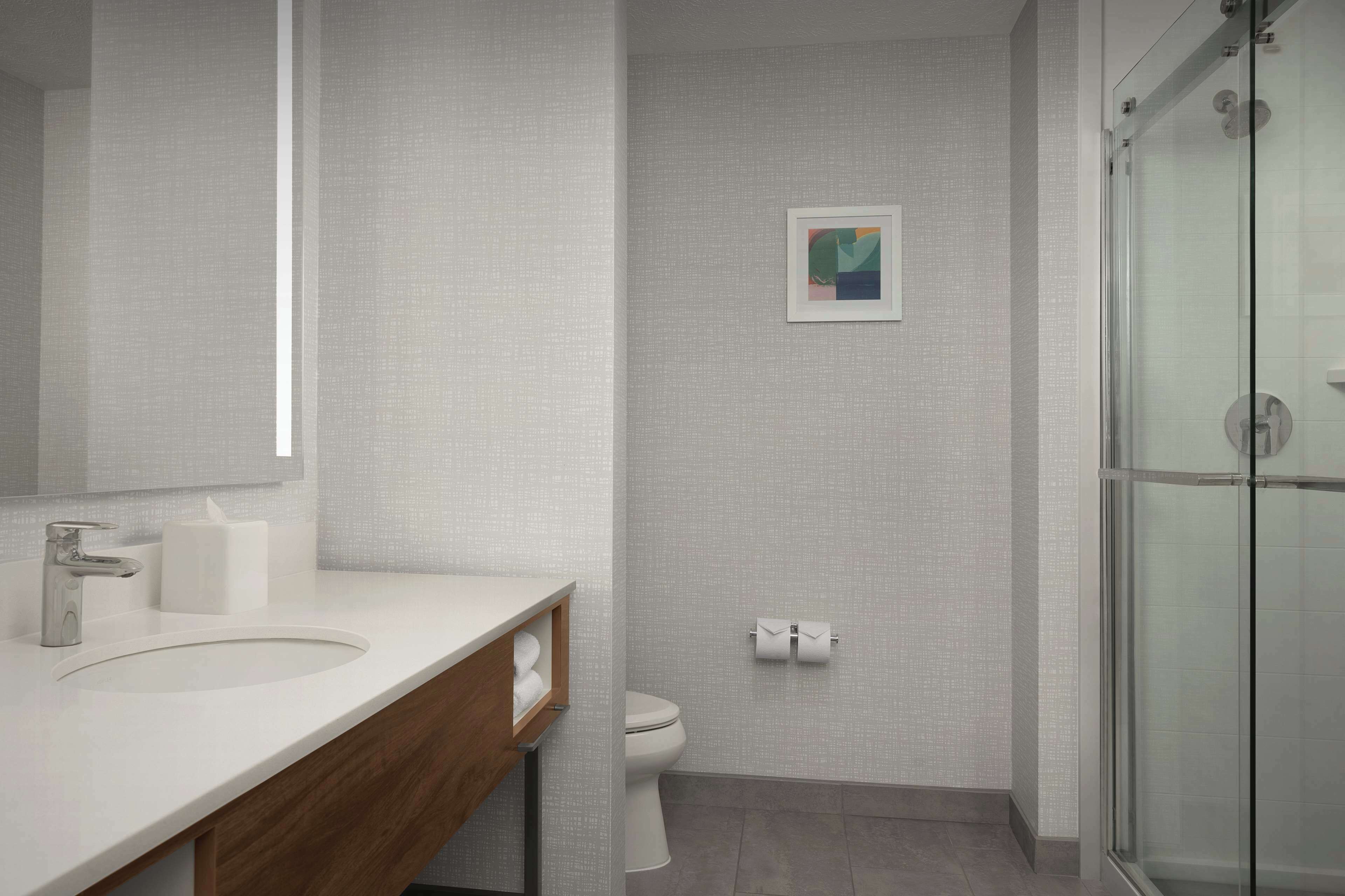 Une salle de bain moderne avec un lavabo blanc, un meuble-lavabo en bois, une cabine de douche en verre et des toilettes.