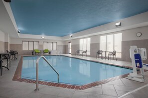An indoor swimming pool with a blue ceiling, tiled floor, and a lifeguard chair.