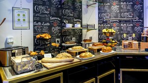 Een toonbank van een koffiezaak met diverse gebakjes en een prikbord waarop koffie en gebakprijzen staan.