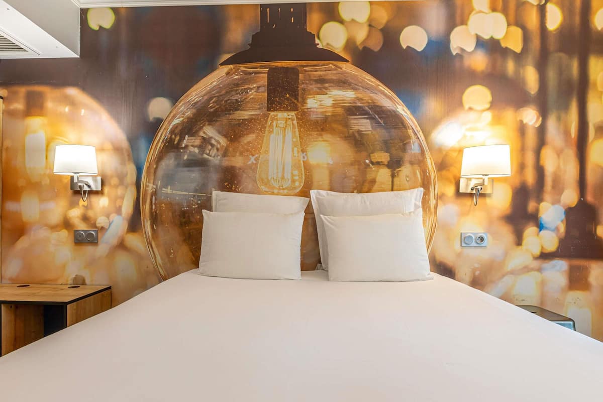 Una cama con dos almohadas blancas, un techo en forma de cúpula transparente y dos lámparas fijadas a la pared.