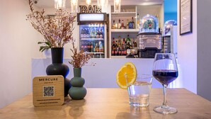 Een barruimte met een houten bord, twee vazen met gedroogde bloemen, een glas water met een schijfje sinaasappel en een glas rode wijn.