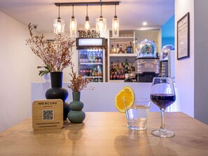 A bar area with a wooden sign, two vases with dried flowers, a glass of water with an orange slice, and a glass of red wine. - Hotel Mercure Paris Malakoff Parc des Expositions (Malakoff)