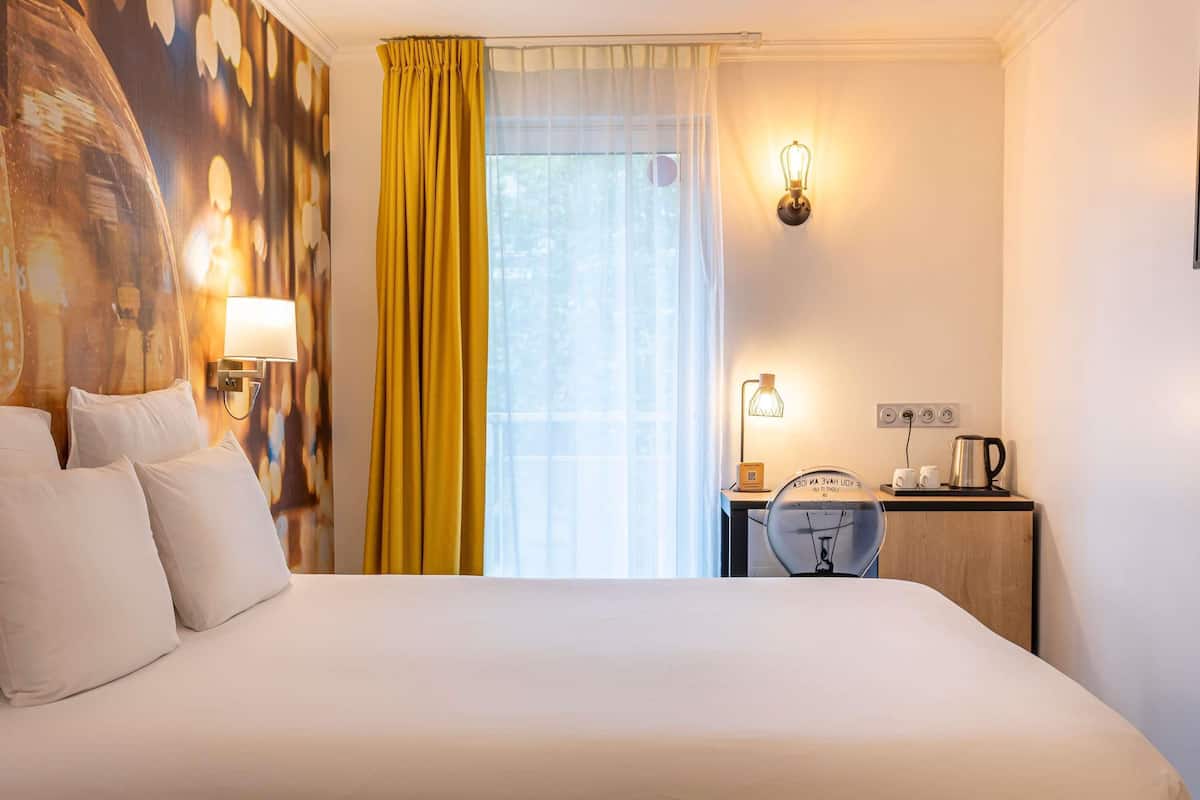 Habitació d'hotel amb un llit gran, escriptori amb làmpada, cadira i vista a l'exterior.