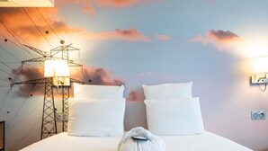 Hotelkamer met een bed, kussens, een handdoek, een muurschildering en een elektriciteitspaal.