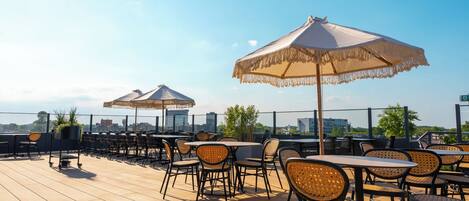 An outdoor seating area with tables and chairs, umbrellas, and a view of the city skyline.