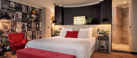 Un dormitorio moderno con una cama grande, una silla roja, una mesita y una zona de ducha.