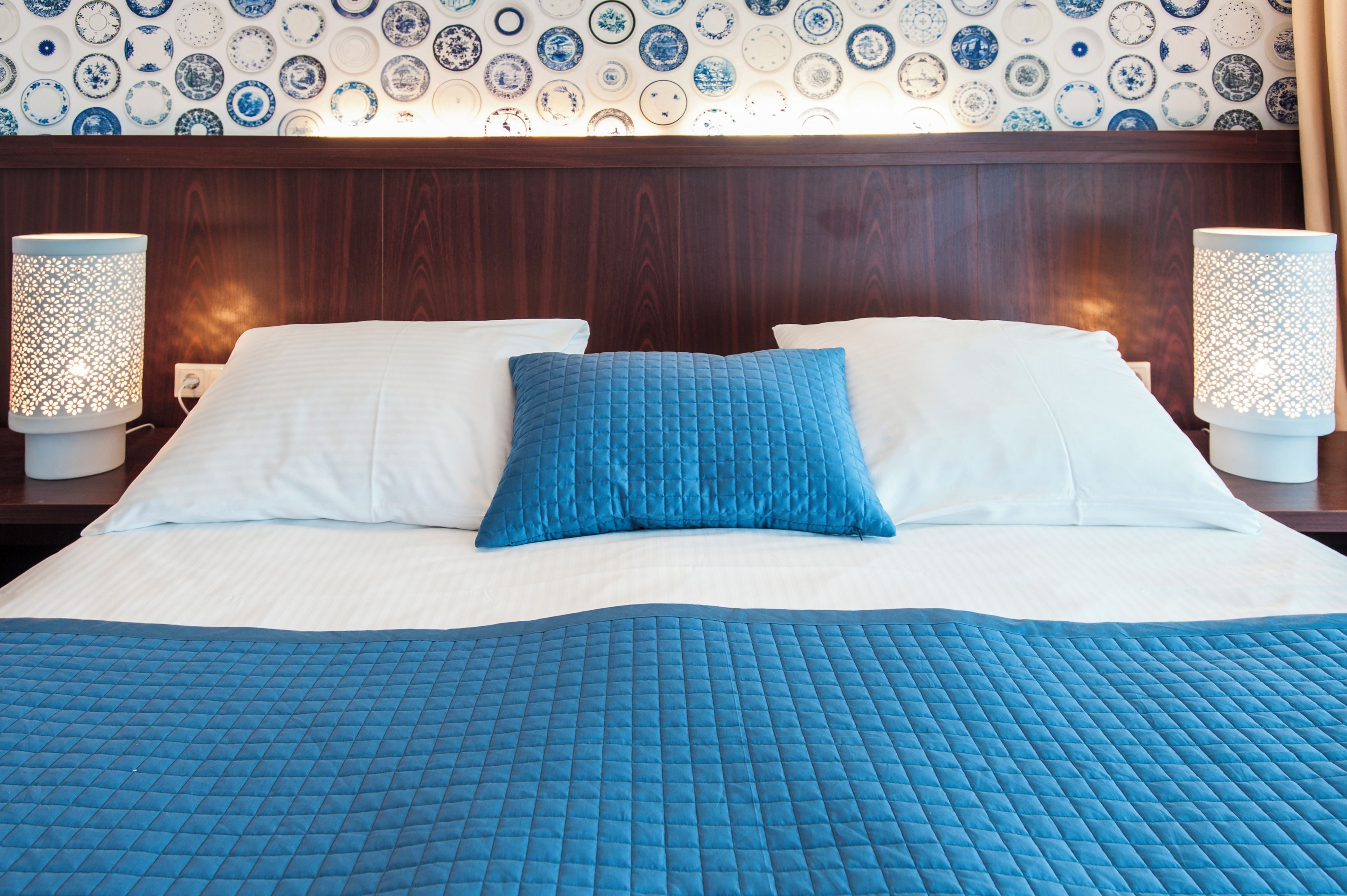 A hotel room with a large bed, white and blue bedding, and a patterned wall.