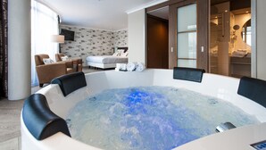 A hotel room with a large bathtub, a bed, a desk, and a wardrobe.