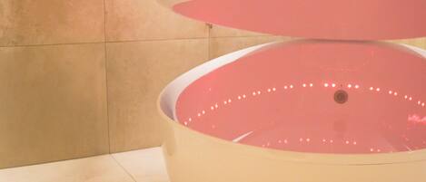 Una estructura circular grande y blanca, con interior rosa, posiblemente una fuente de agua, en una habitación con baldosas e iluminación en el techo.