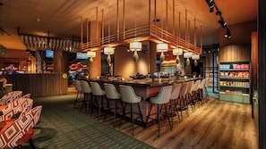 Zona de bar con diversas opciones de asientos, incluyendo taburetes y sillas, y una barra con variedad de aperitivos y bebidas.